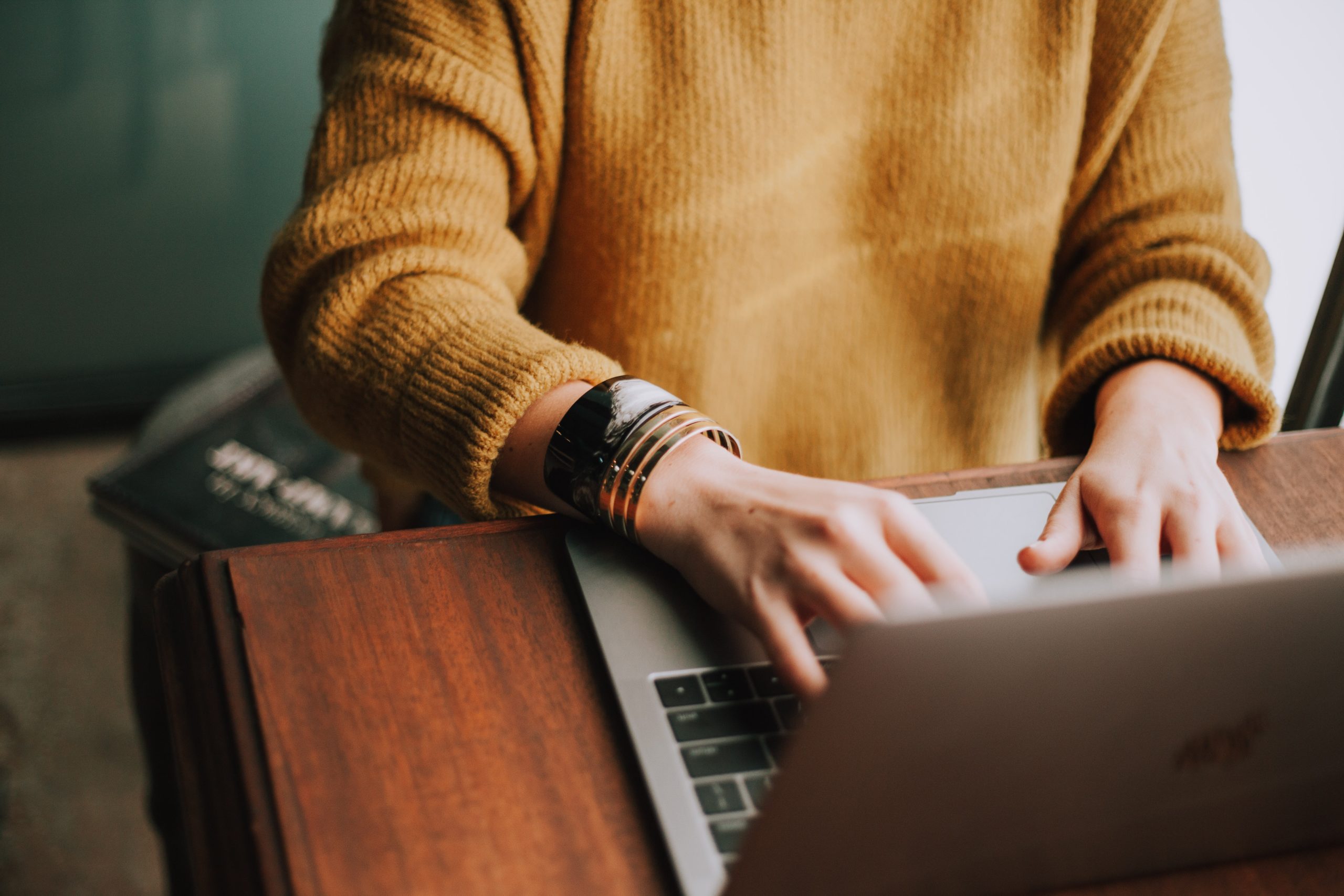 Person in a yellow sweater tying at a laptop