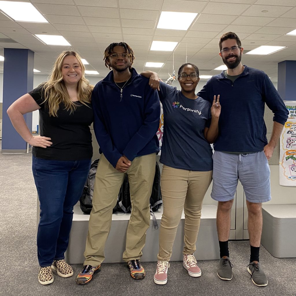 Group of employees in an office setting posing for a photo wearing casual attire